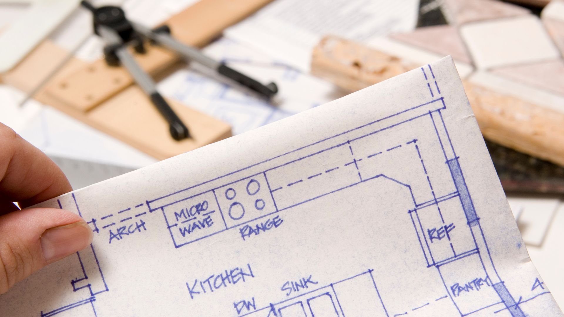 Hand holding kitchen layout blueprint with architectural drafting tools